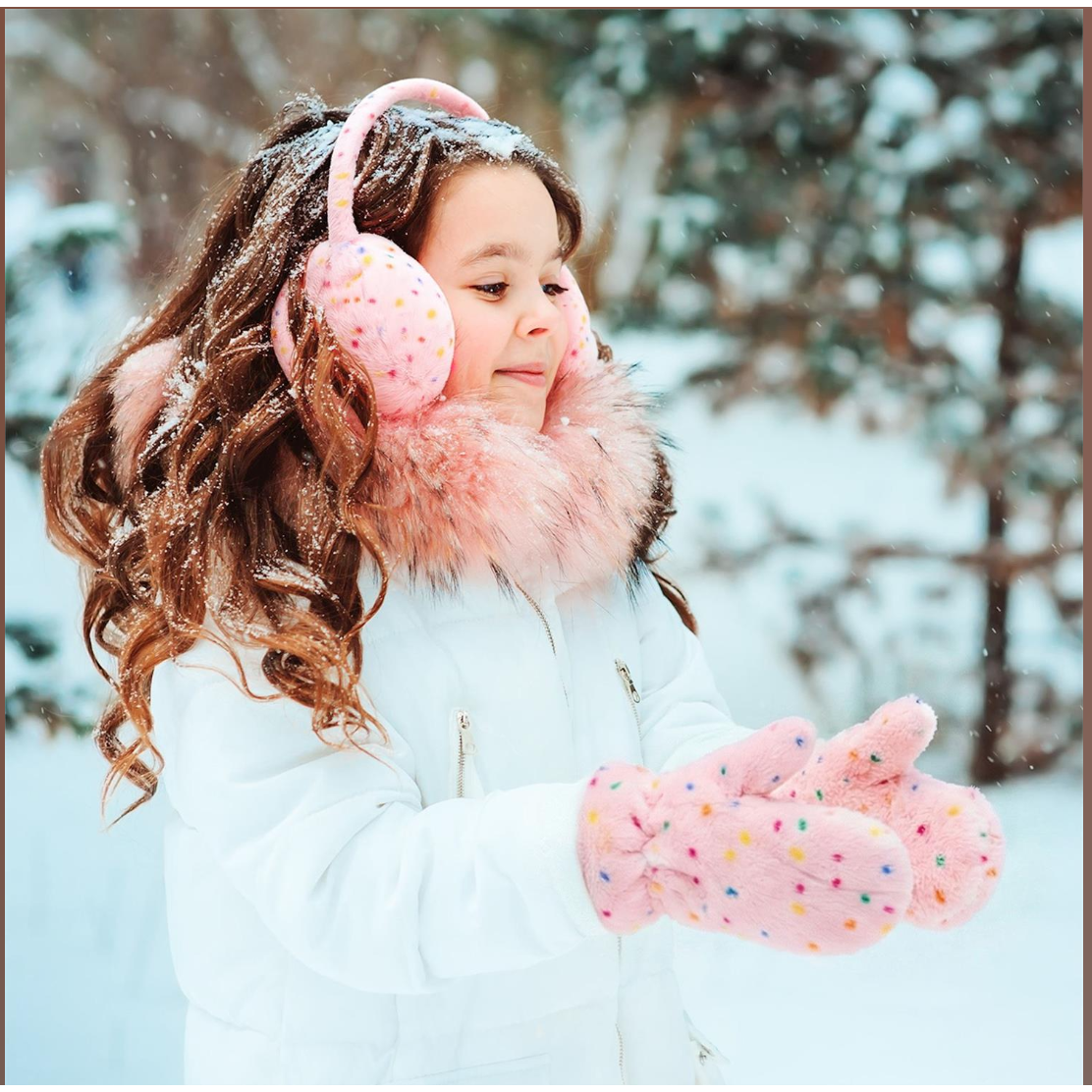 Child in winter clothing with pink earmuffs and gloves in a snowy setting