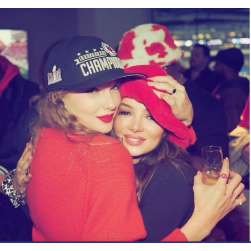 Two people hugging, one wearing a championship cap and the other in a red outfit, with a blurred background.