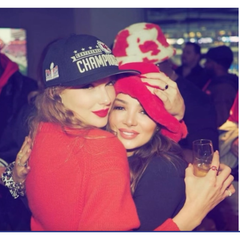 Two people hugging, one wearing a championship cap and the other in a red outfit, with a blurred background.