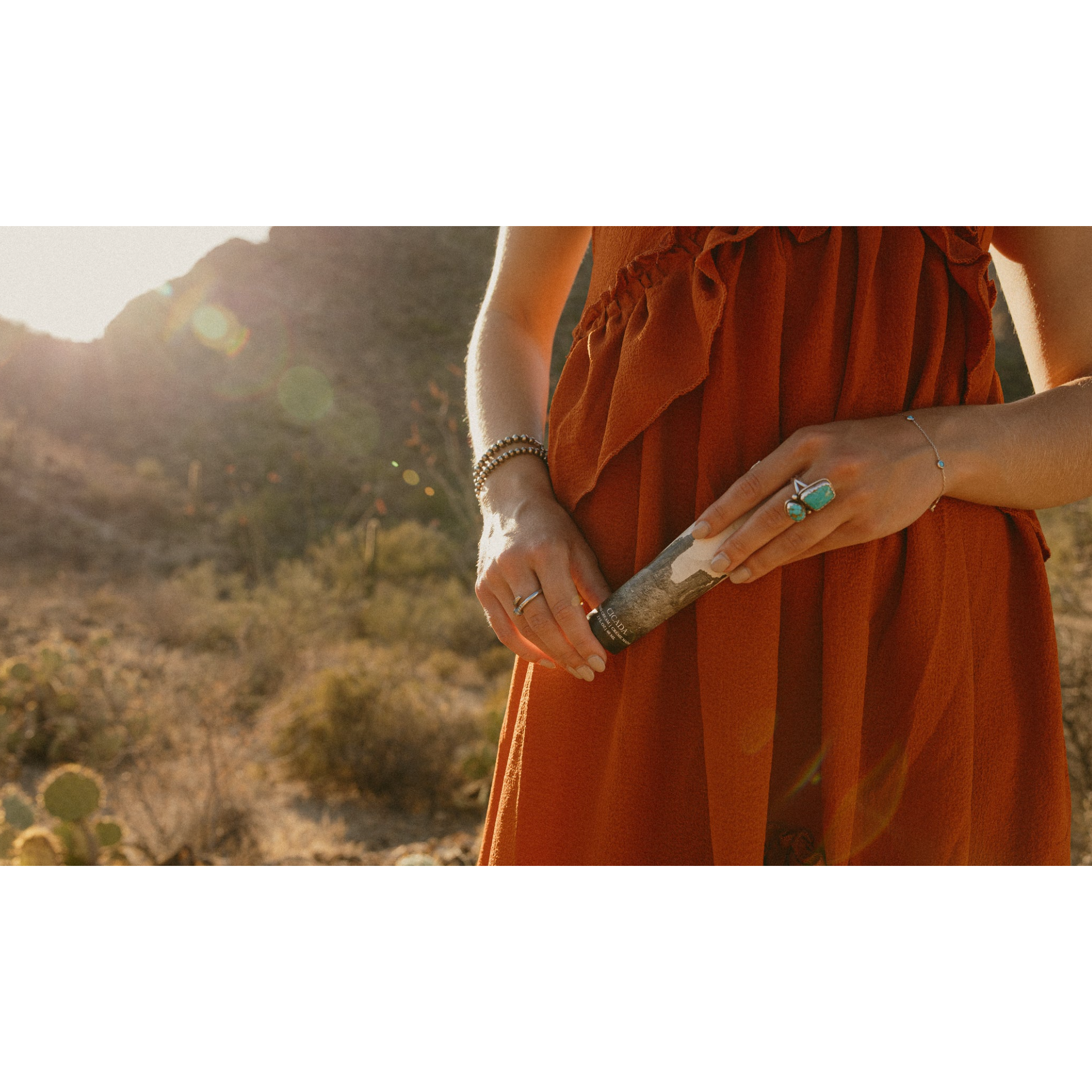 Person in an orange dress holding a cactus in a desert setting