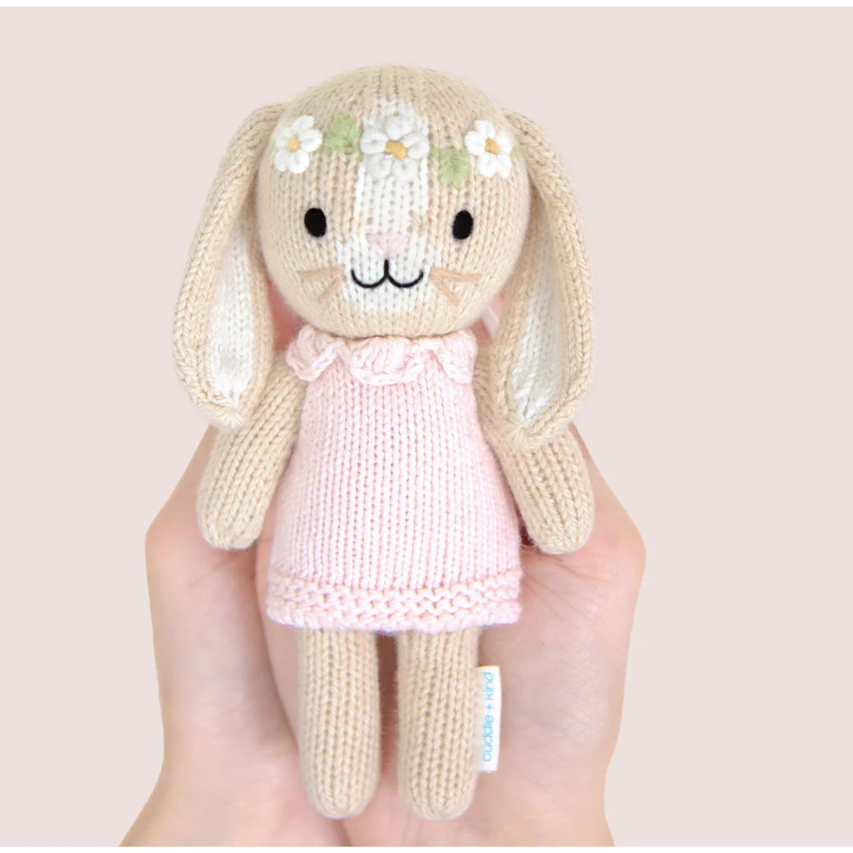 Knitted bunny toy with a pink dress held in a hand against a light background