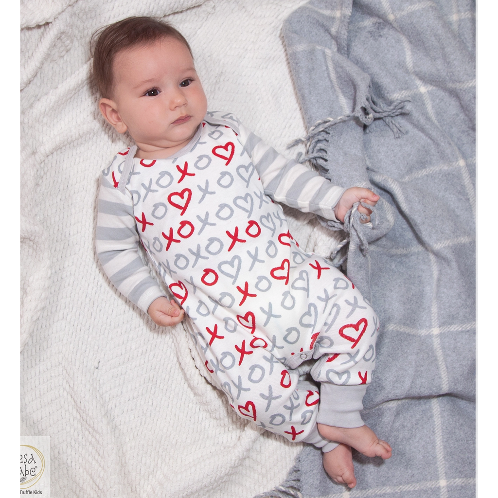 Baby in a white outfit with red and gray patterns, lying on a soft surface.