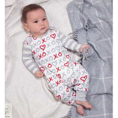 Baby in a white outfit with red and gray patterns, lying on a soft surface.