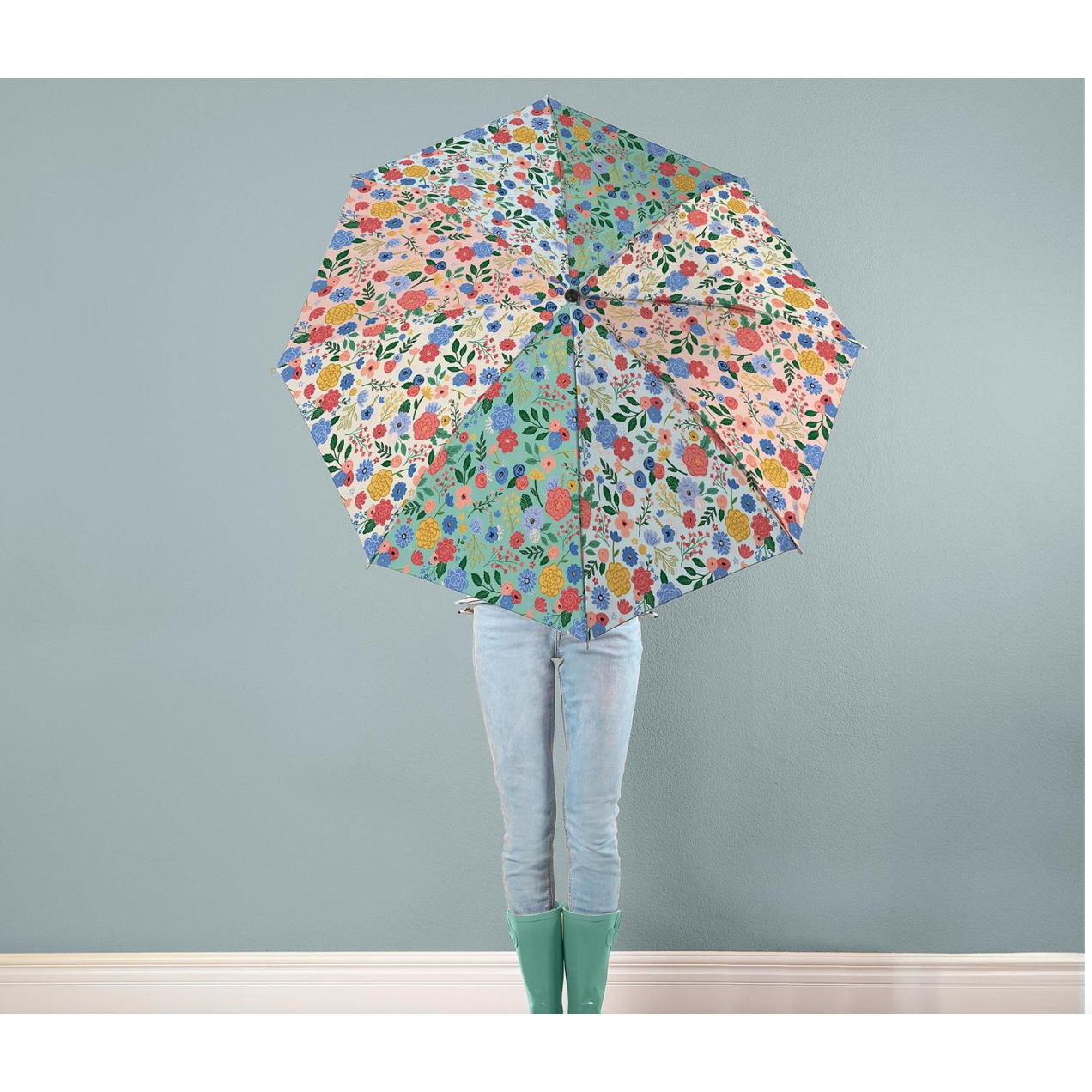Person holding a large floral umbrella against a plain wall