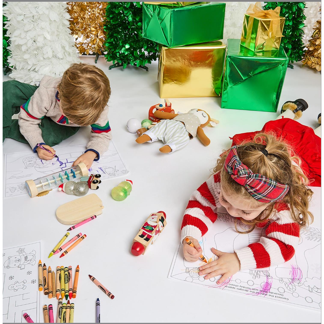 Two children coloring at a table with Christmas decorations and presents.