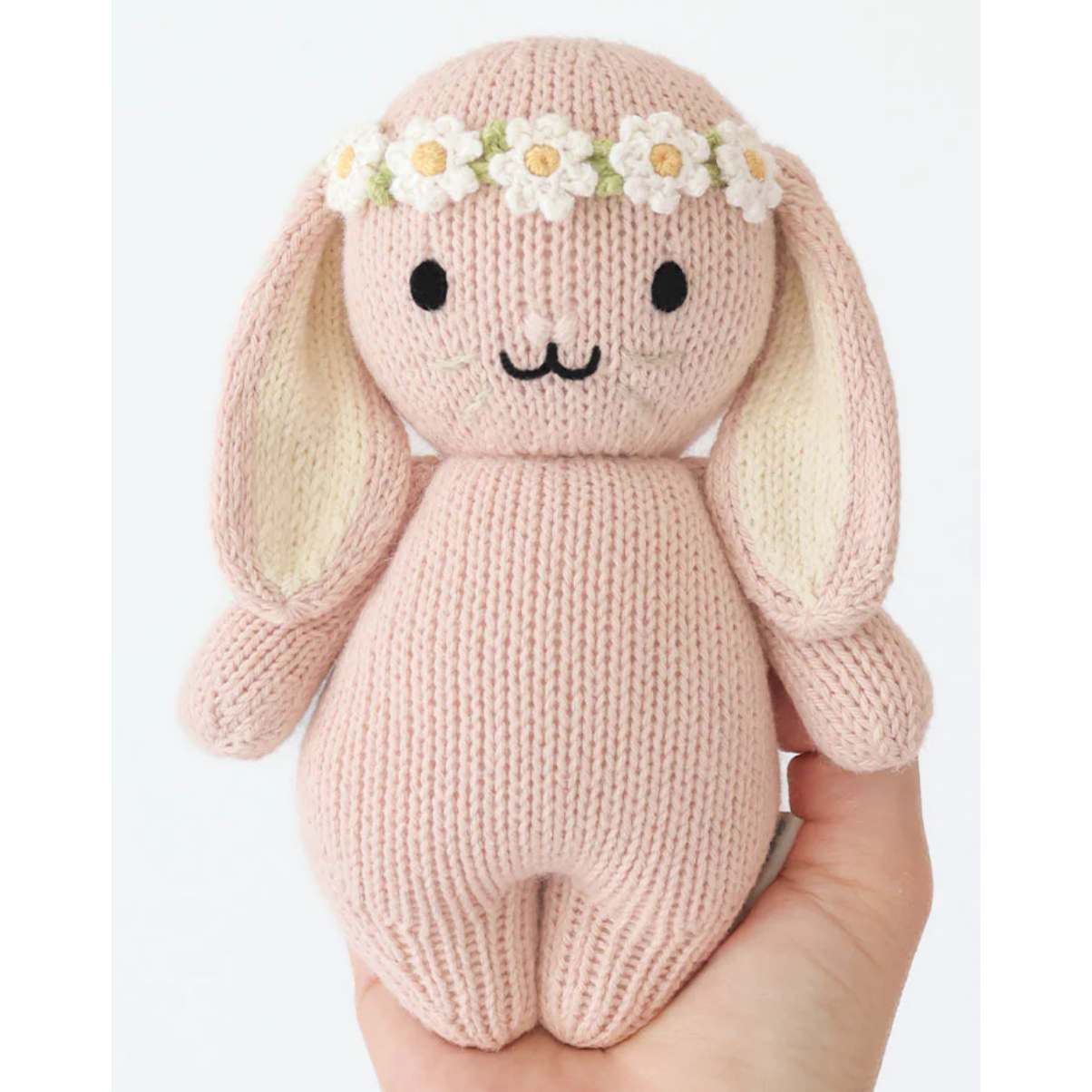 Knitted bunny toy with a flower crown held in a hand against a white background