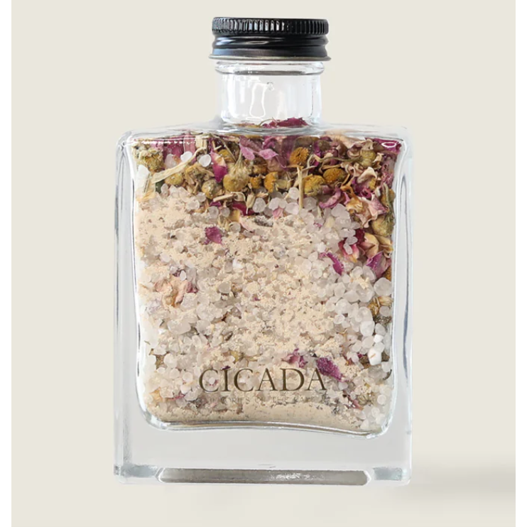 Glass jar with bath salts and flowers labeled 'CICADA' on a beige background