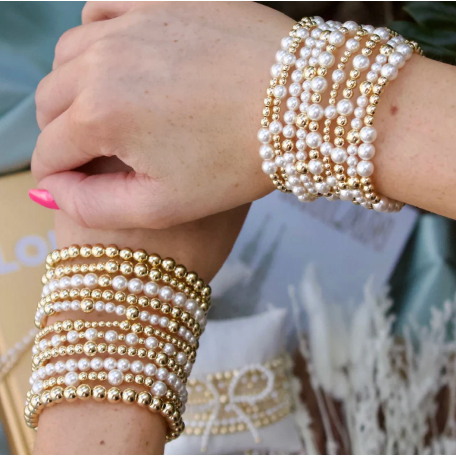 Close-up of a hand wearing multiple pearl and gold beaded bracelets.