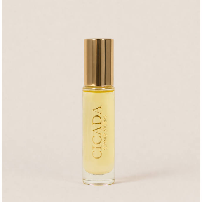 A clear glass perfume bottle with pale yellow liquid and a metallic gold cap, standing upright on a light beige background. The bottle is labeled 'CICADA SUMMER STORMS'.