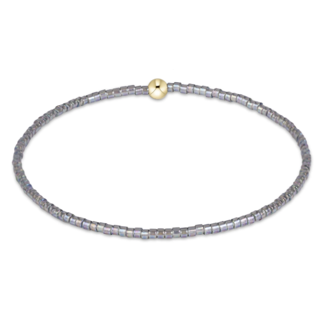 A beaded stretch bracelet made of small iridescent gray beads with a single gold-toned round bead, shown on a plain white background.