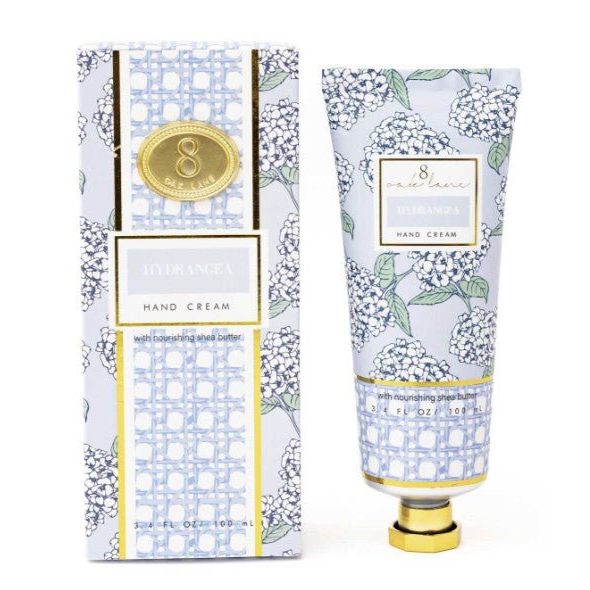A tube of 8 by Jolie Hydrangea hand cream with a gold cap stands next to its matching patterned box.