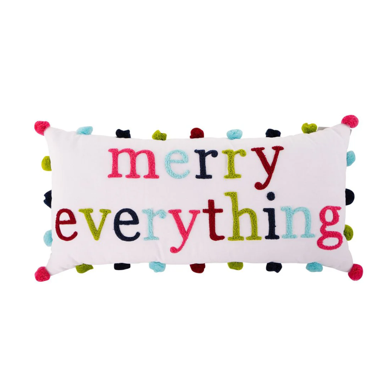 Decorative pillow with 'merry everything' text and colorful pom-poms on a white background