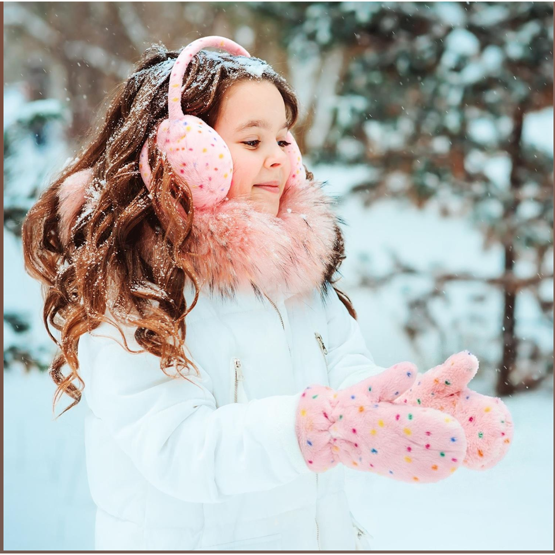 Child wearing pink earmuffs and gloves in a snowy setting