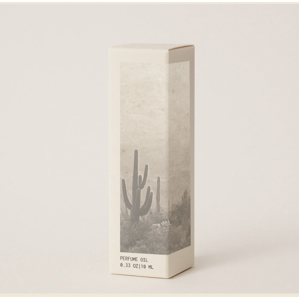 A tall rectangular box of perfume oil with a minimalist desert landscape illustration featuring a saguaro cactus, set against a solid light beige background.