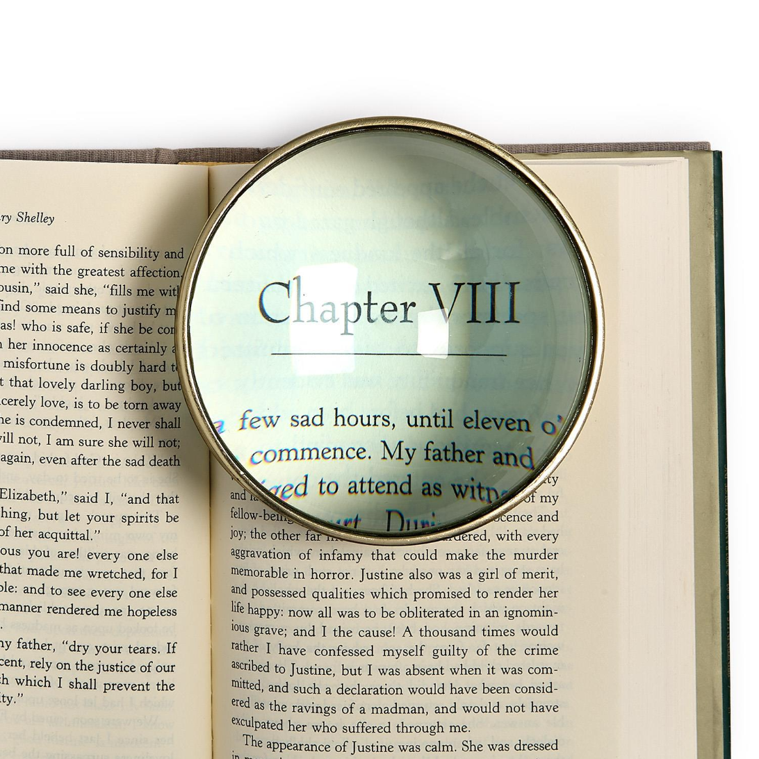 A rectangular magnifying glass with a clear lens and light wood frame, shown over a printed book page with the heading 'Chapter VIII' enlarged under the magnifier.