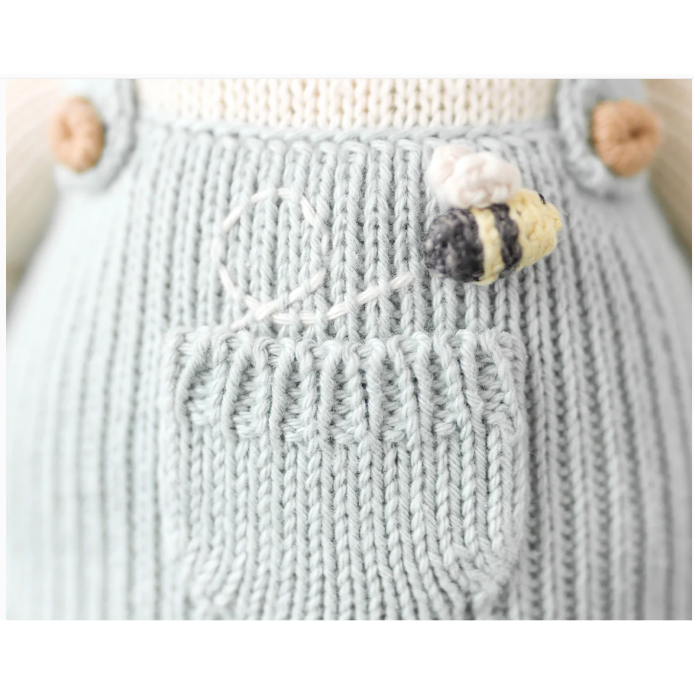 Close-up of a knitted garment with a bee pin on a neutral background