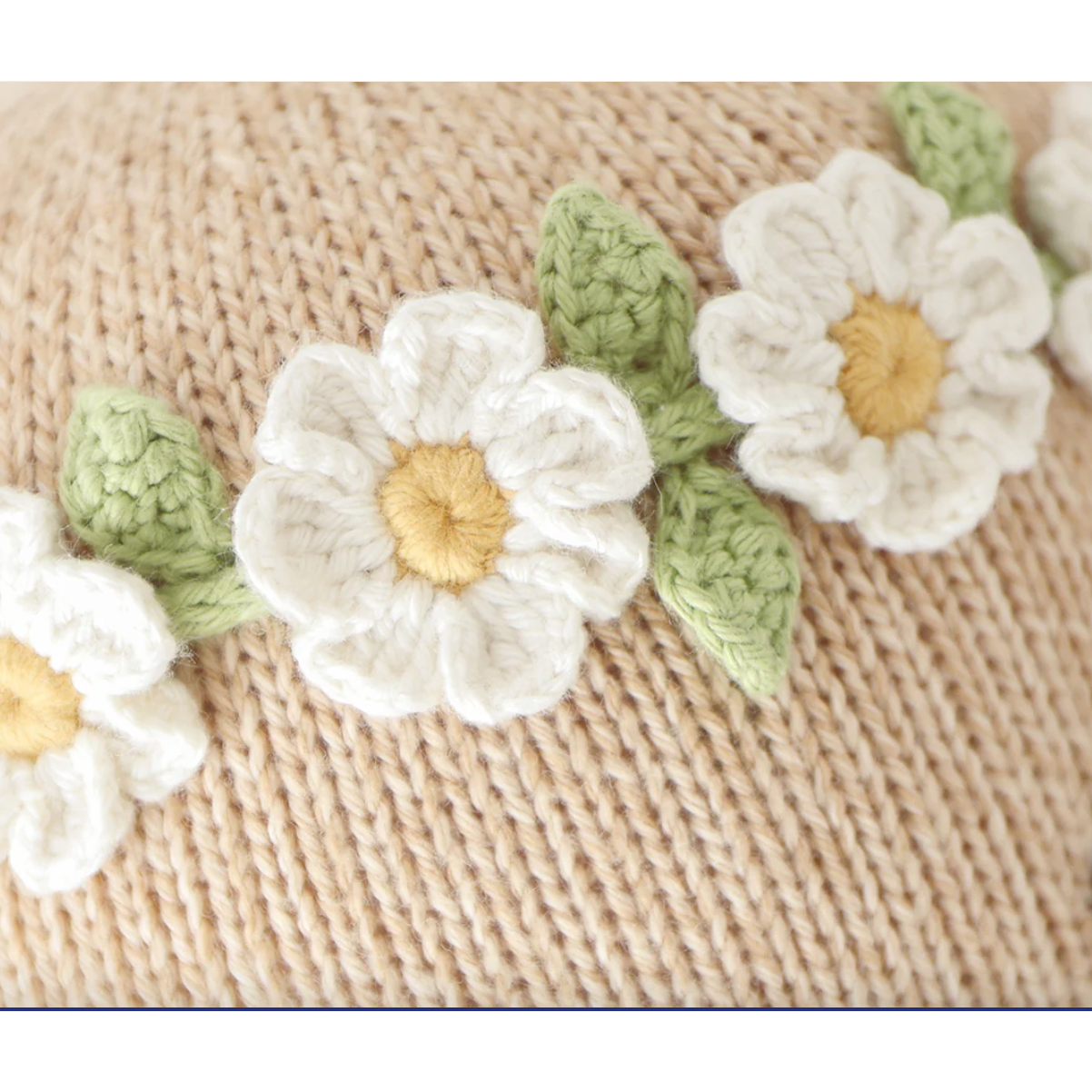 Crocheted white flowers with green leaves on a textured beige background