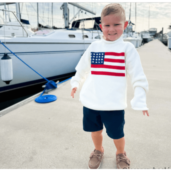 Child wearing a white sweatshirt with an American flag design at a marina.