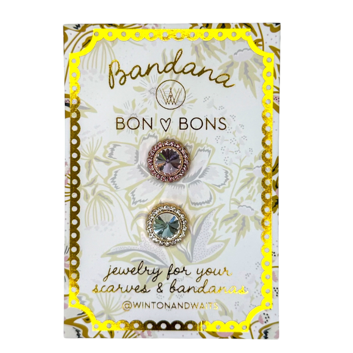 Two round jewelry pieces displayed on a branded Winton & Ways Bandana card. The card has a white floral background with a bright yellow scalloped border and gold script text reading 'Bandana BON BONS jewelry for your scarves & bandanas @WINTONANDWAYS'.