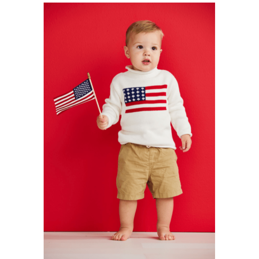 Child wearing a white sweater with an American flag design, holding a small American flag against a red background.