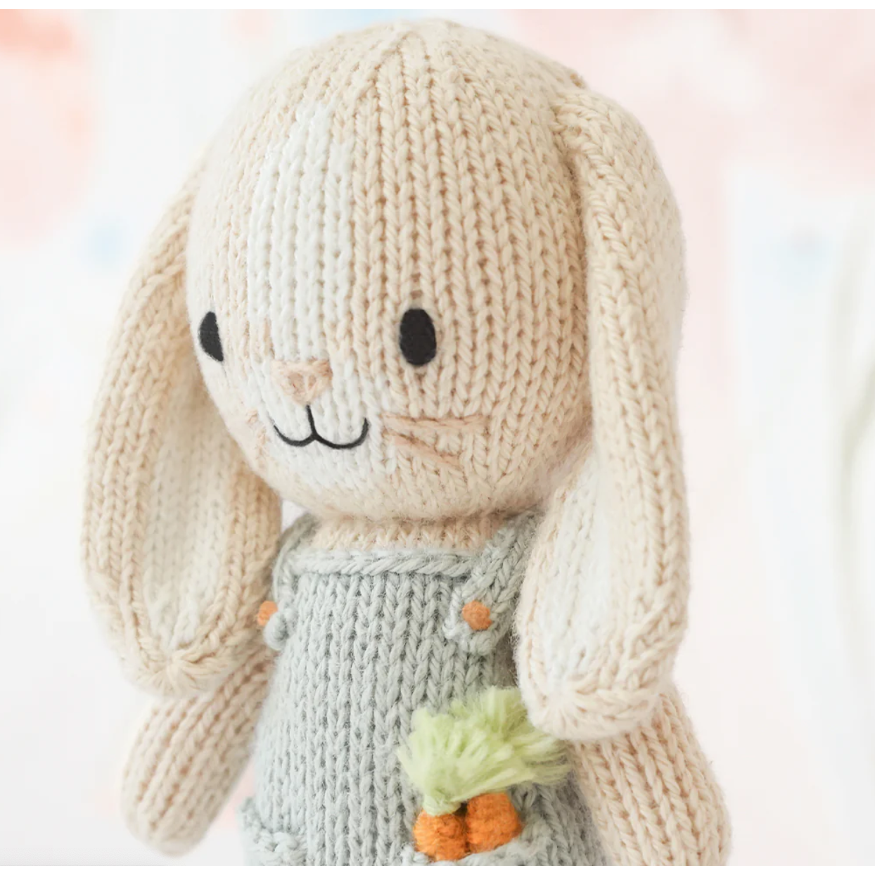 Knitted bunny toy with a carrot on a soft pink background