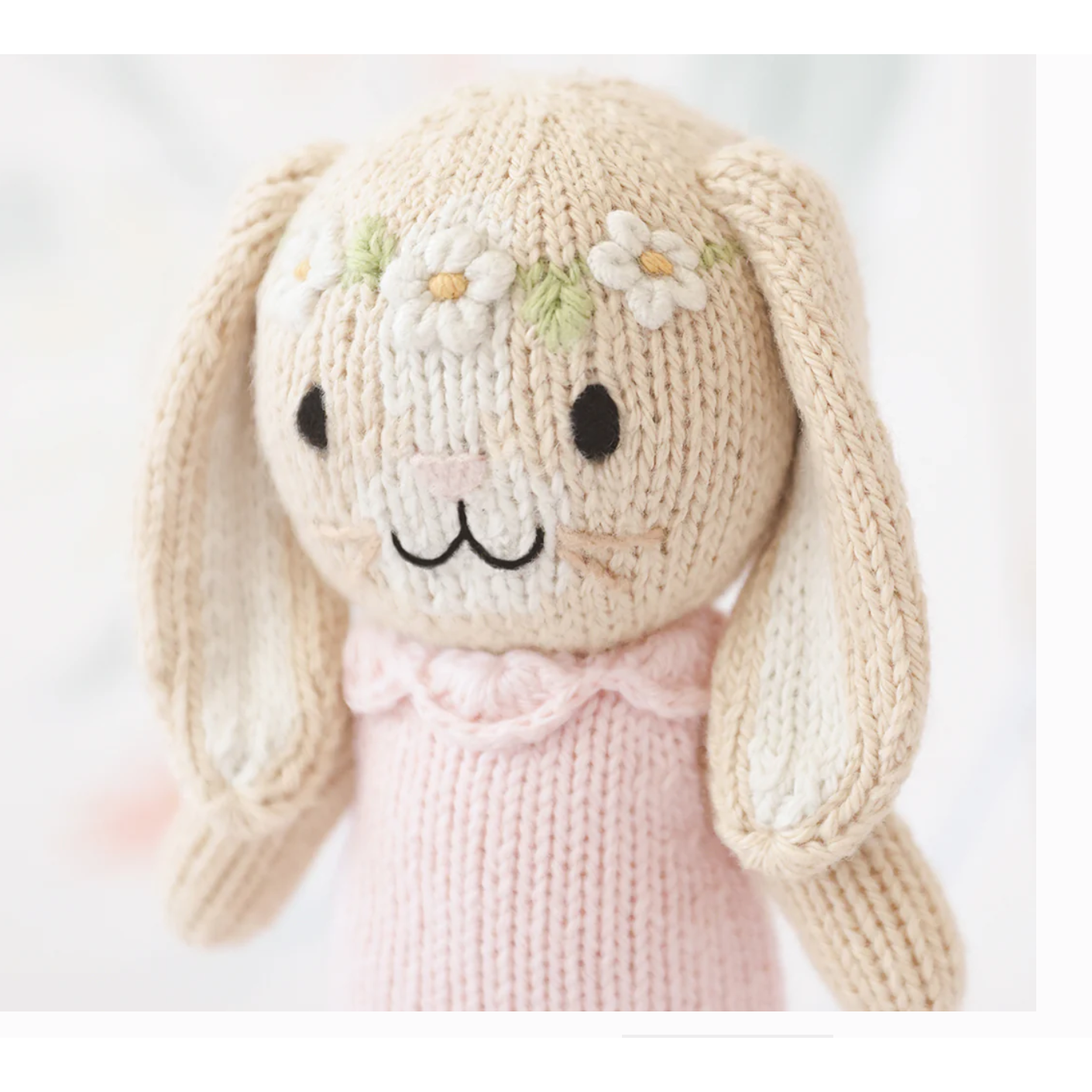 Knitted bunny toy with a pink dress on a white background
