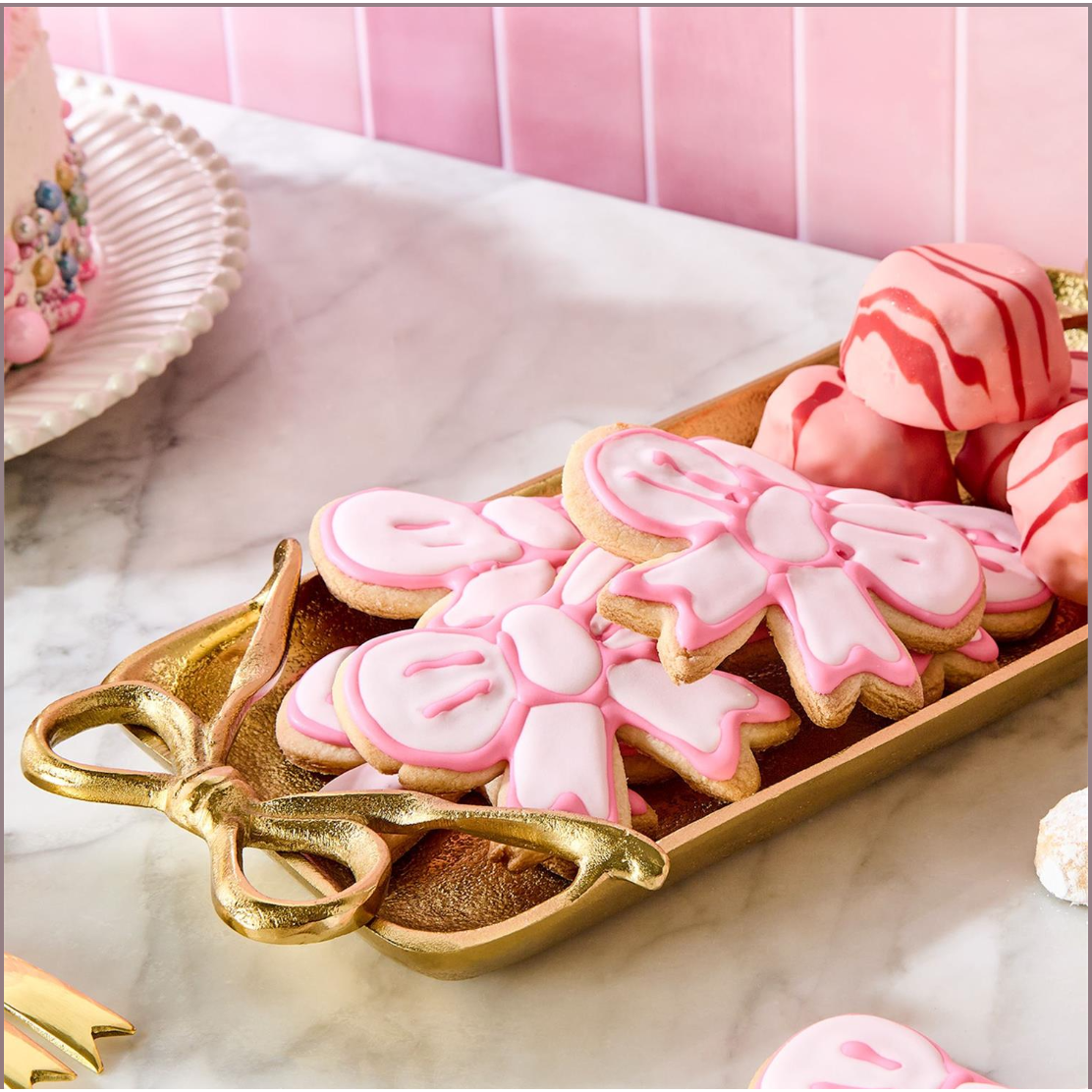 Decorative cookies with pink icing on a gold tray against a pink background