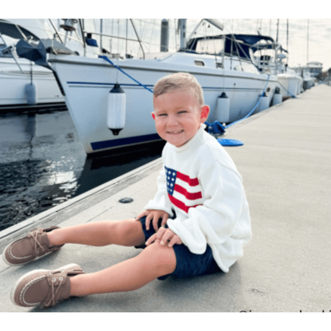 Child sitting on a dock by a marina with boats in the background