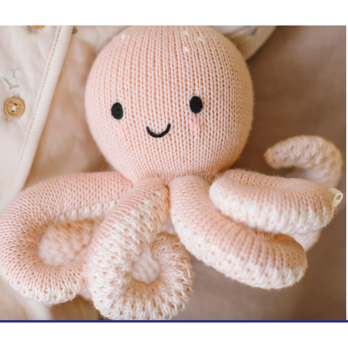 Knitted octopus toy with a smiling face held by a person wearing a beige jacket.