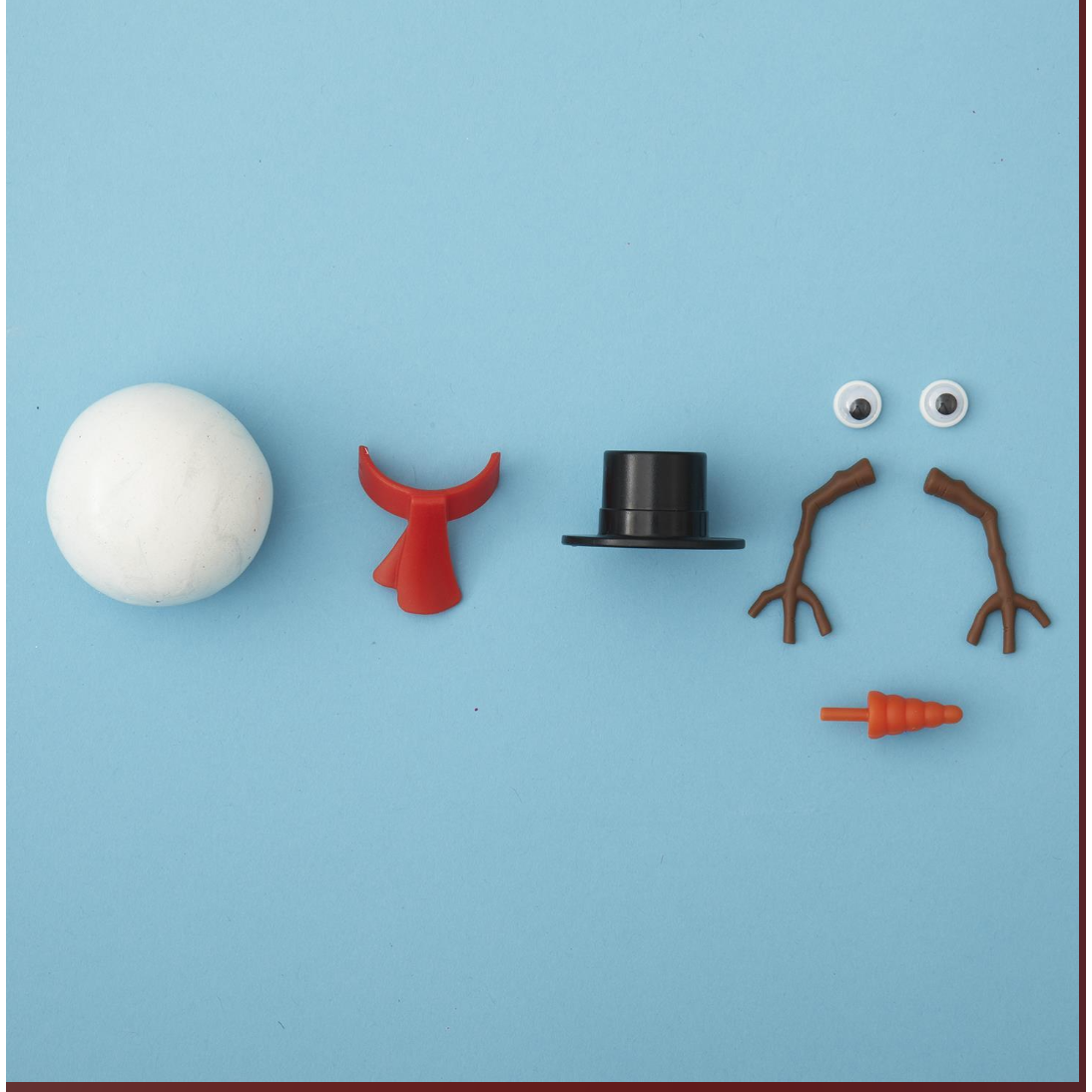 Set of toy parts including a white ball, red tail, black top hat, brown branches, and orange carrot on a blue background.