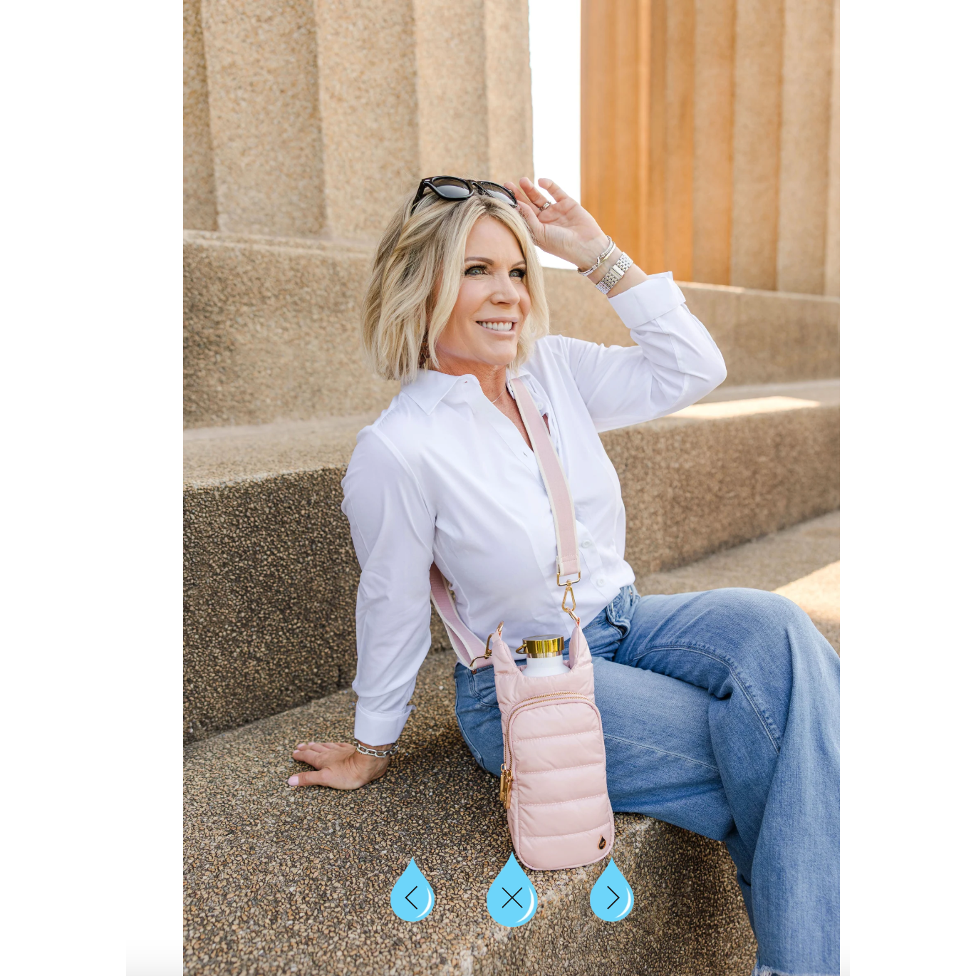 Woman sitting on steps wearing a white shirt and blue jeans, holding a pink puffer bag.