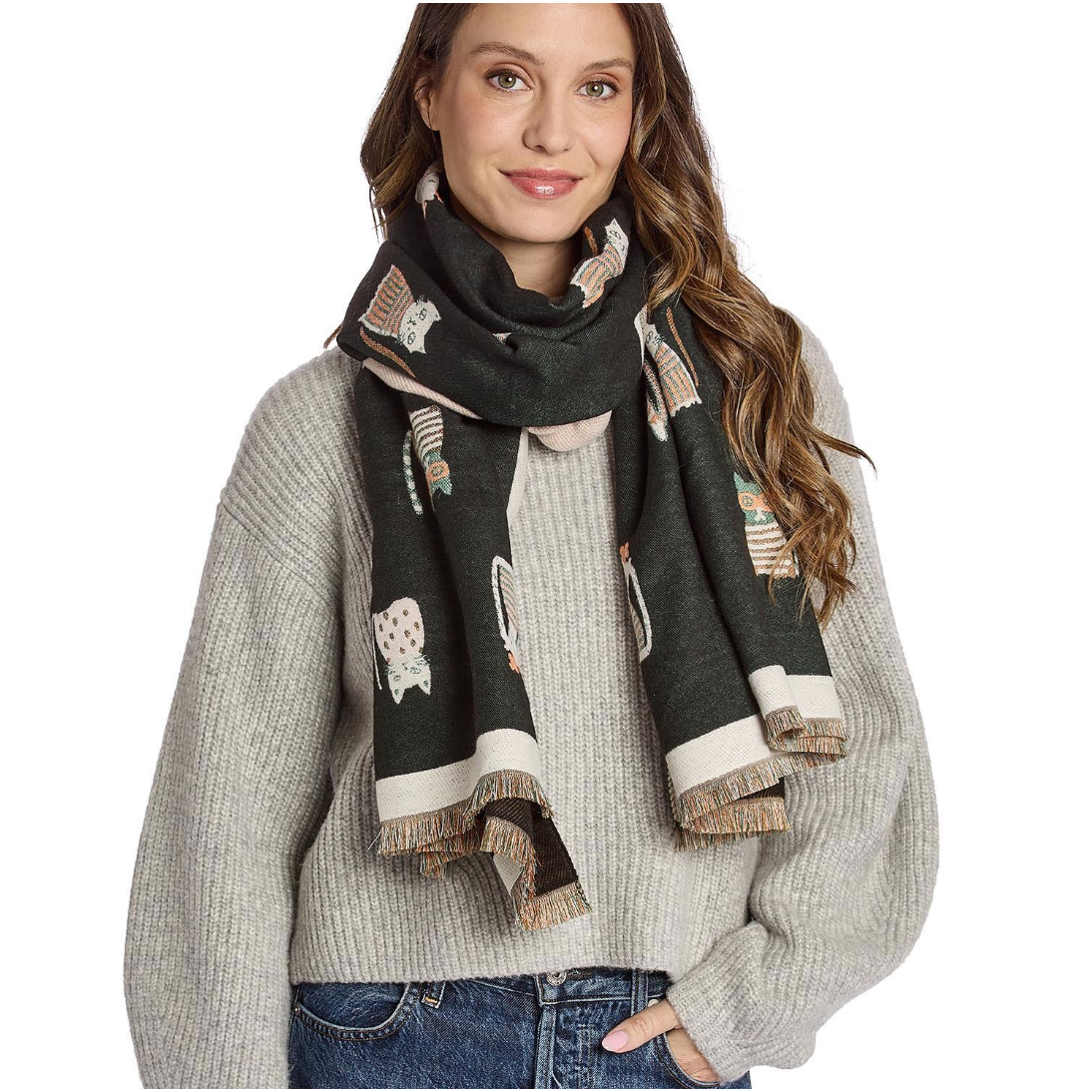 A woman wearing a dark green knit scarf with a pattern of small cartoon animals and cream-colored fringed edges, paired with a light gray ribbed sweater and blue jeans, against a plain white background.