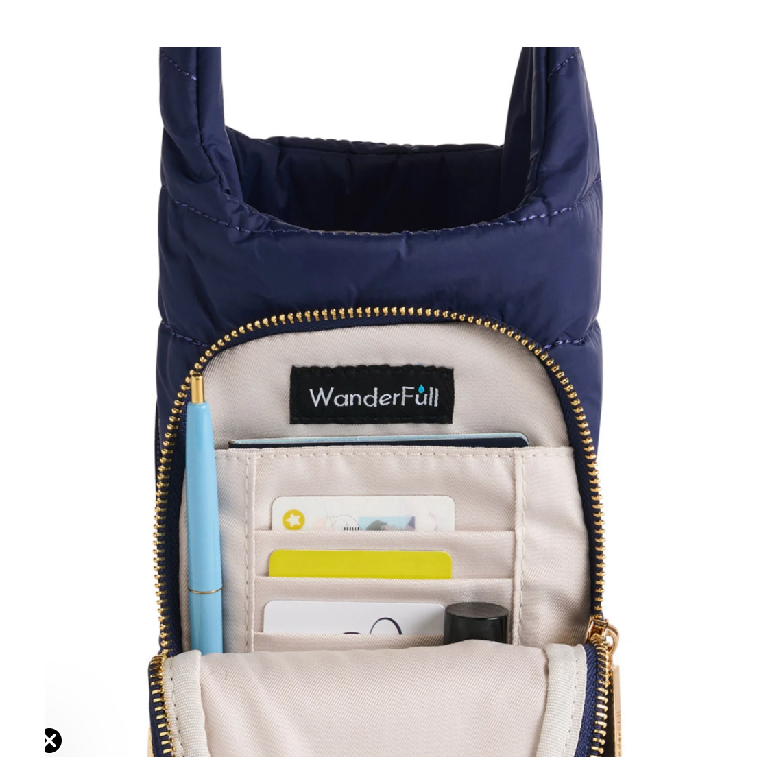 Navy blue crossbody bag with gold zipper, containing stationery items, on a white background.