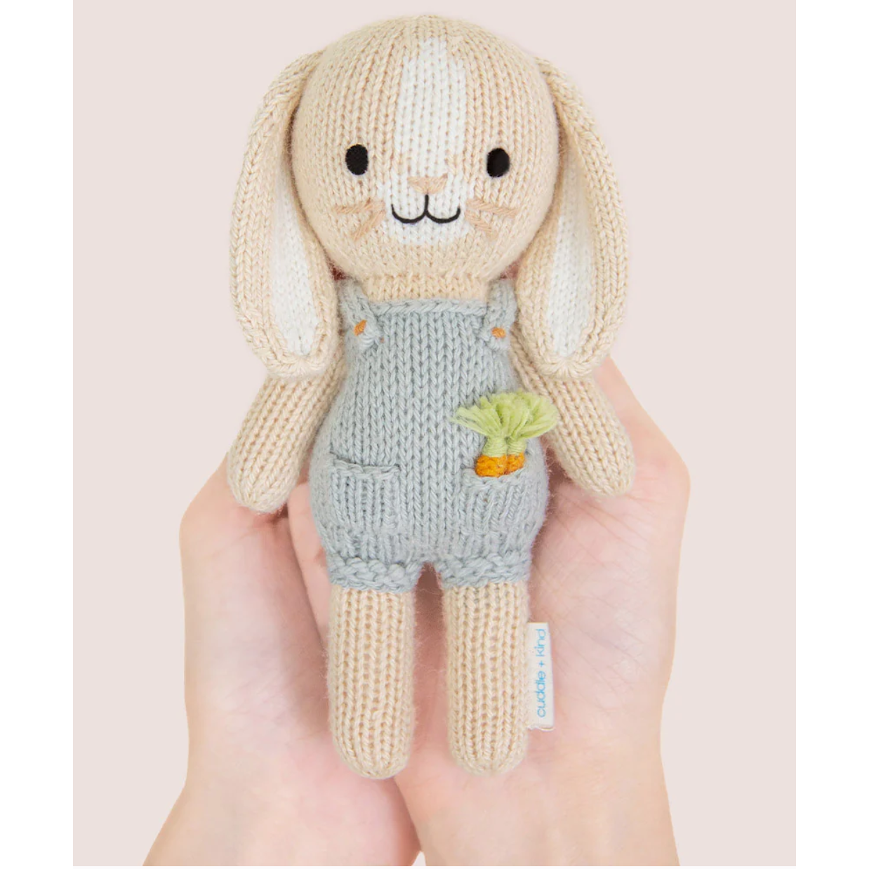 Knitted toy rabbit held in a hand with a plain background