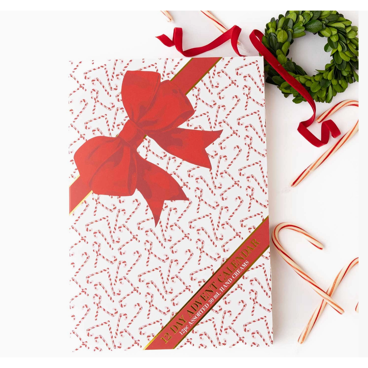 A Christmas advent calendar with a white background, red dotted candy cane pattern, and a large red bow on the front. The calendar is styled with red ribbons, candy canes, and a green wreath on a white background.