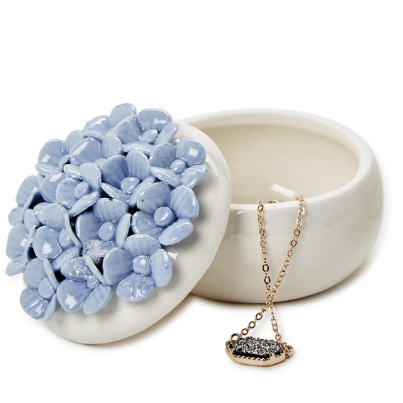 Necklace with a pendant inside an open white container, next to a pile of blue stones.