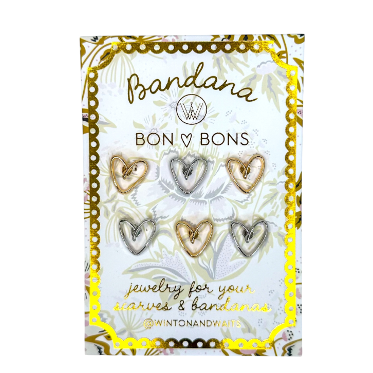 A package of six heart-shaped pins displayed on a decorative white and gold card. 