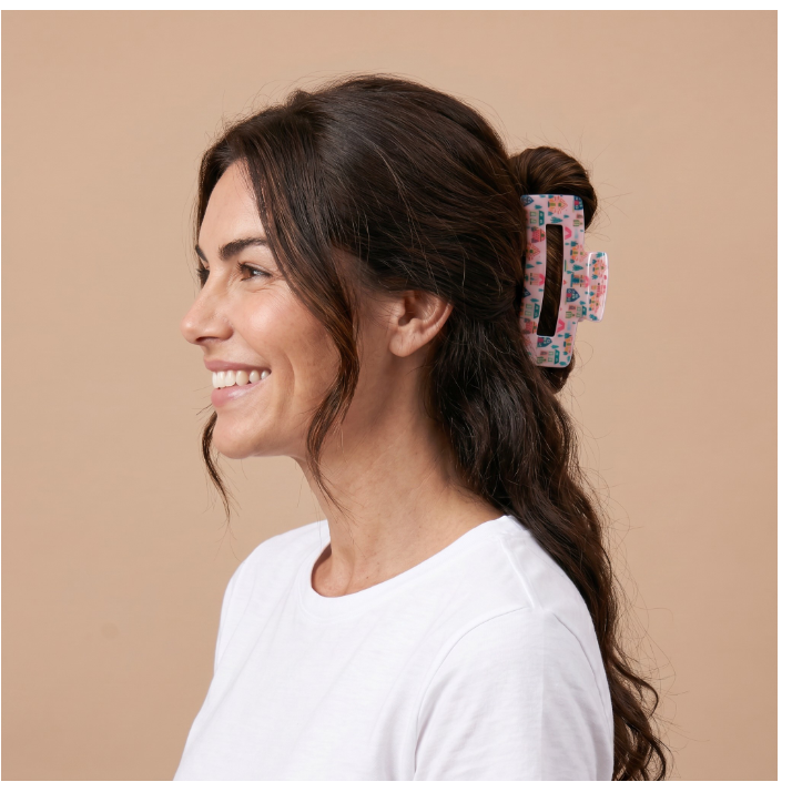 A woman with dark brown hair tied back in a low bun wearing a colorful floral-patterned claw clip, shown in profile against a solid beige background.