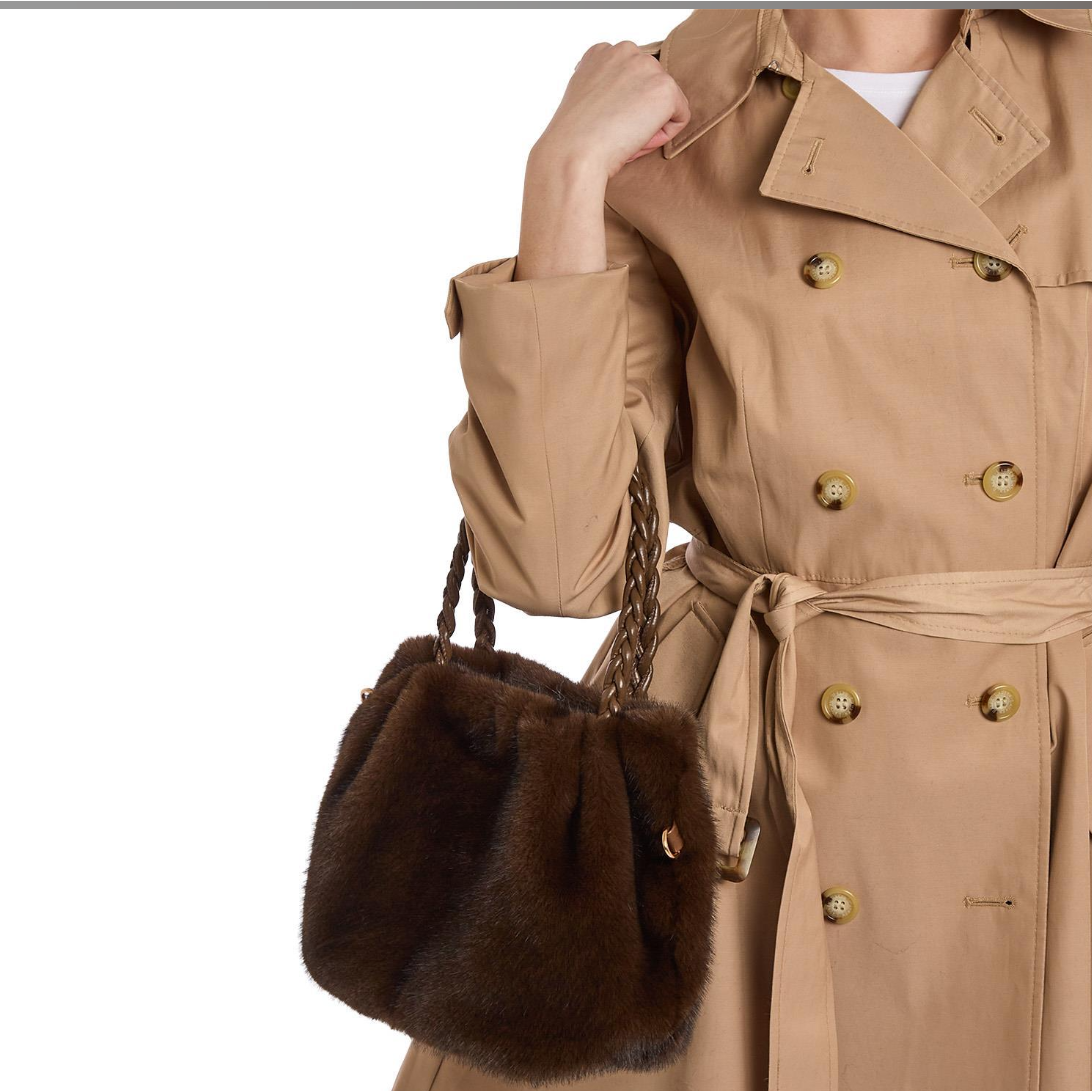 Person wearing a beige trench coat holding a brown fur handbag on a white background