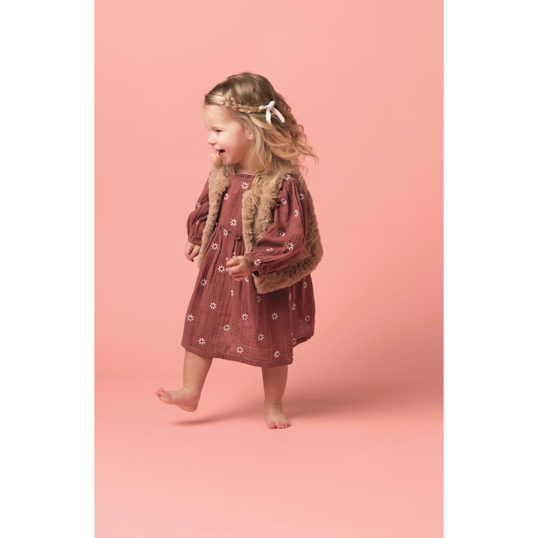 Young girl in a floral dress with fur trim against a pink background