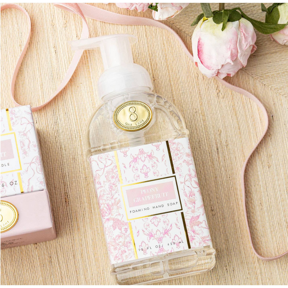 Foaming hand soap bottle with floral design on a wooden surface with pink ribbon and flowers.
