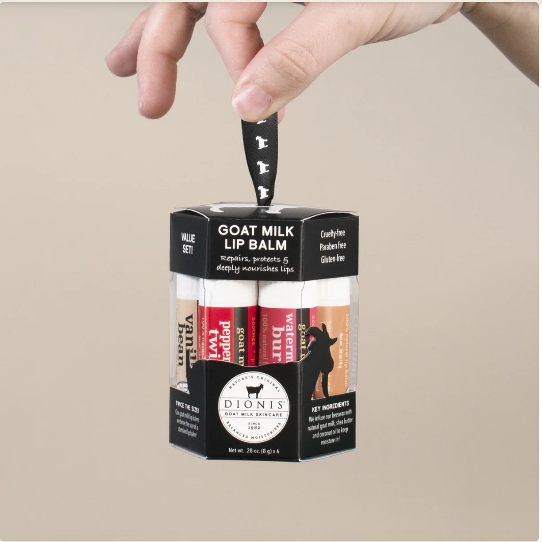 Box of goat milk lip balm with a hand lifting one out on a beige background
