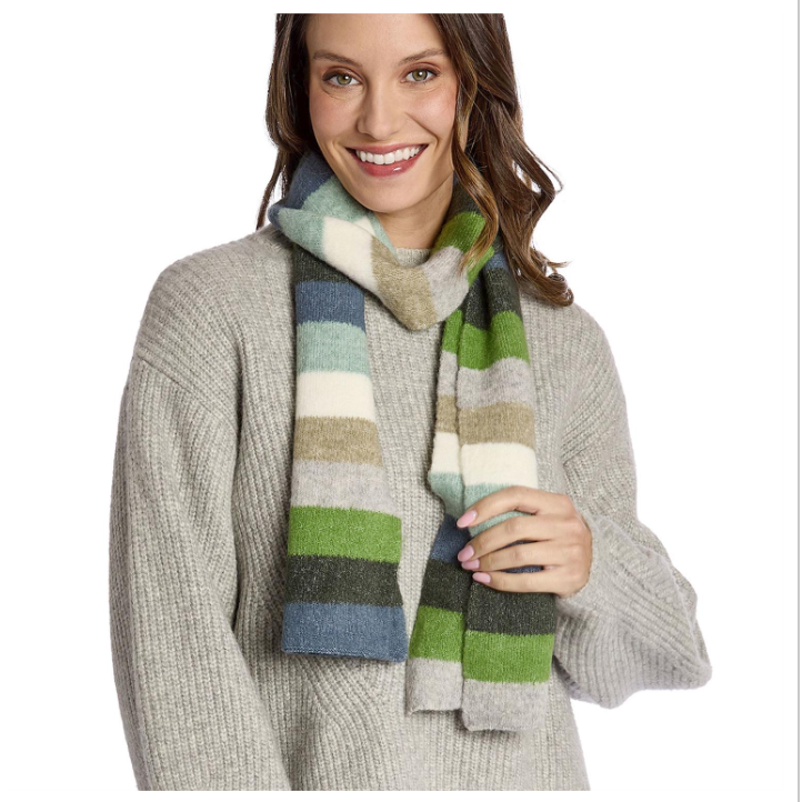 A woman wearing a chunky knit light gray sweater and a thick striped scarf in shades of green, blue, cream, and beige, set against a plain white background.