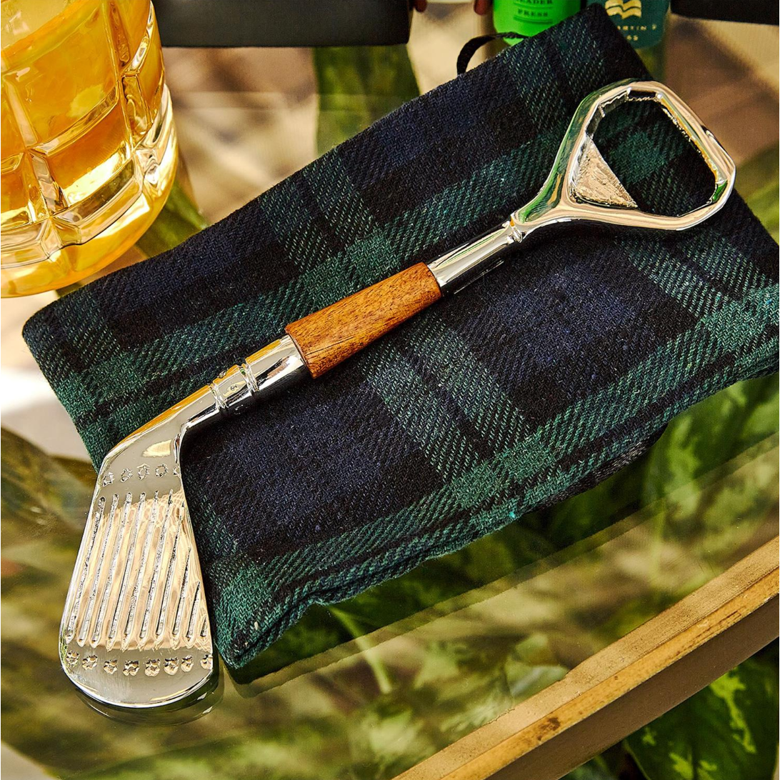 Golf club and bottle opener on a plaid cloth with a glass of beer in the background