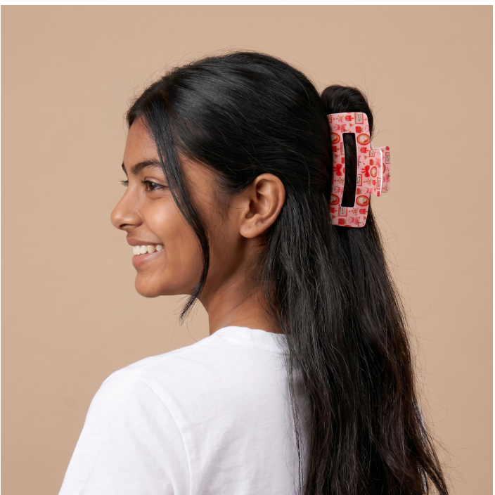 A woman with long black hair wearing a red and white patterned claw clip, shown in profile against a solid beige background.