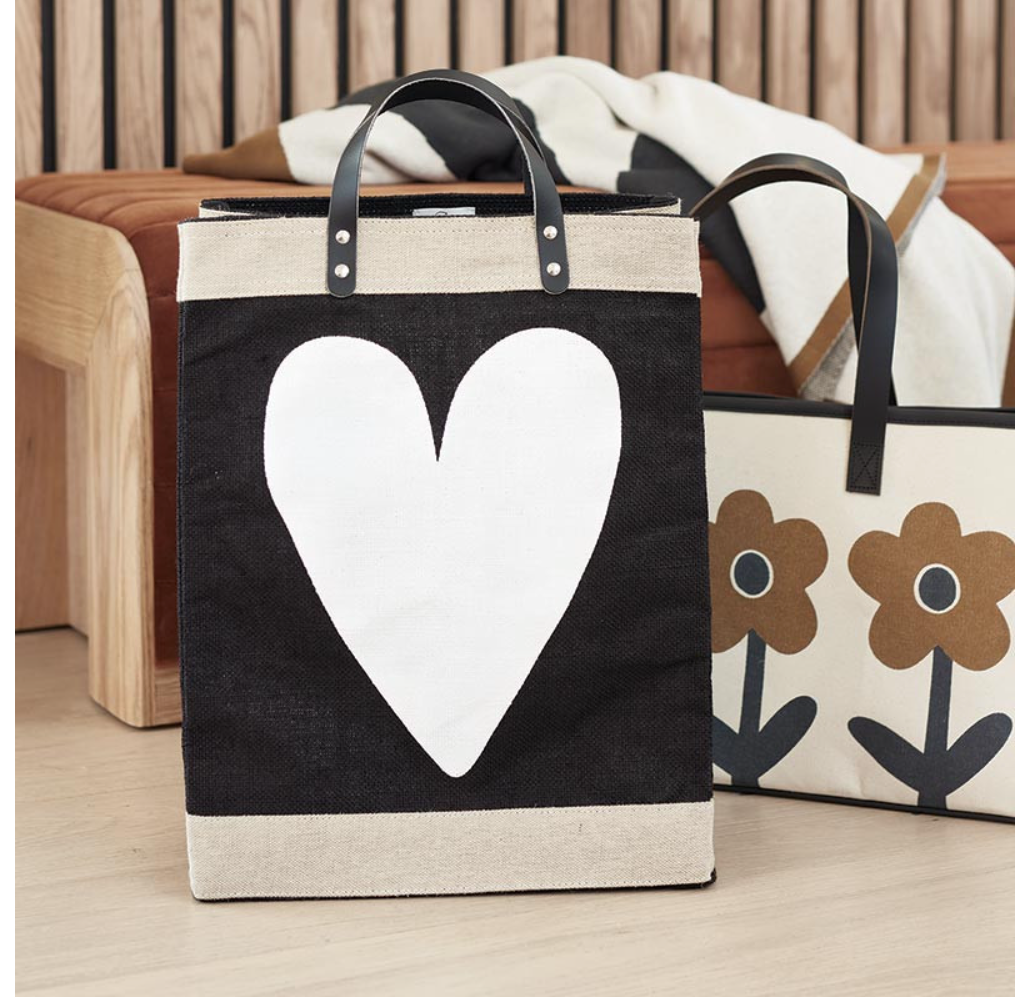 Black tote bag with a white heart design on a wooden surface.