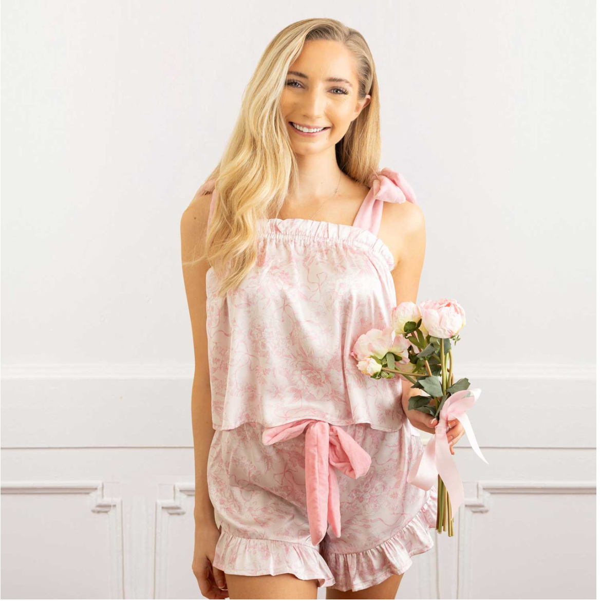 Woman wearing a pink outfit holding flowers against a white background