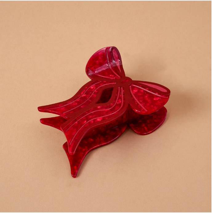 A translucent red hair claw clip shaped like a bow, shown on a solid beige background.