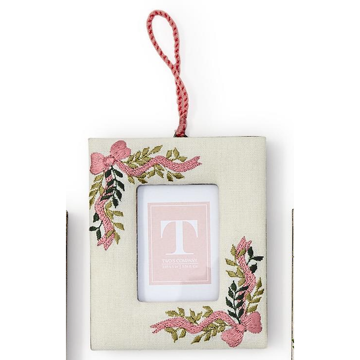 A square fabric picture frame ornament with a hanging loop, featuring embroidered pink ribbons, green leaves, and a central cutout holding a pink card with a monogram letter T.
