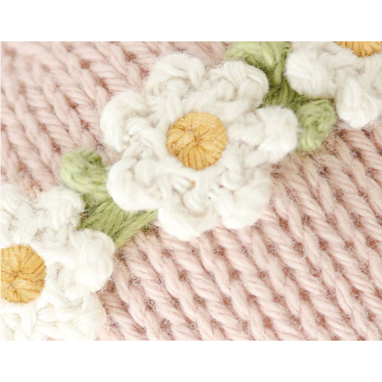 Close-up of knitted fabric with embroidered white flowers and green leaves.